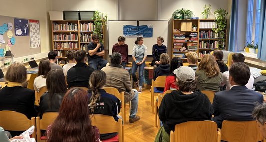 Vier Personen sprechen vor Gruppe in Bibliothek