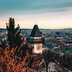 Eine atemberaubende Luftaufnahme von Graz mit dem ikonischen Uhrturm, umgeben von üppigem Laubwerk in der Dämmerung.