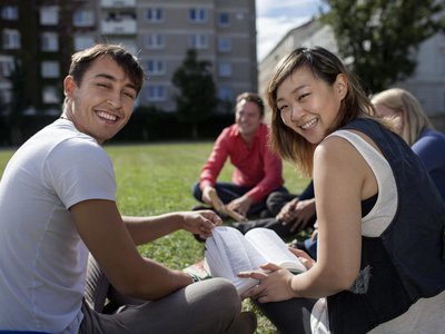 Studenten sitzen mit Büchern auf der Wiese und lachen fröhlich