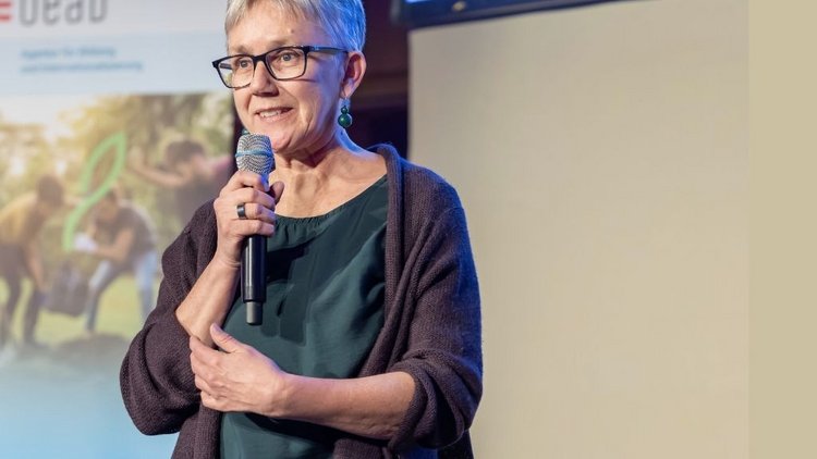 Frau mit Mikrophon in der Hand sprechend im Hintergrund Roll-Up