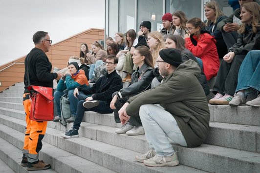 Gruppe junger Menschen sitzt auf Stiege und hört altem Mann zu