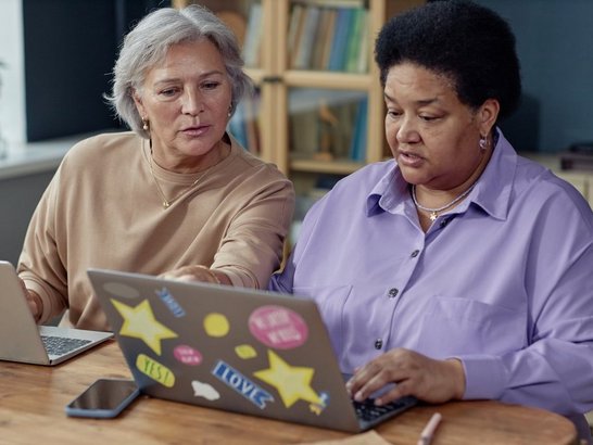 Zwei ältere Damen sitzen gemeinsam vor den Laptops