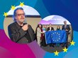 Zwei Fotos vor bunten Hintergrund mit gelben Sternen: Ein Bild mit Mann mit Bart und längerem Haar in Anzug mit Mikro, Gruppenbild mit mehreren Personen, die EU-Flagge halten