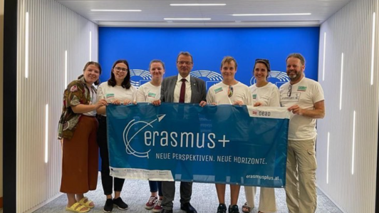 Gruppe an sieben Menschen hält Erasmus+ Banner in die Kamera