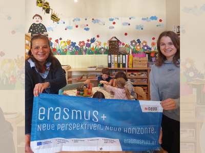 Zwei Frauen halten einen Erasmus+ Banner in die Kamera und lachen 