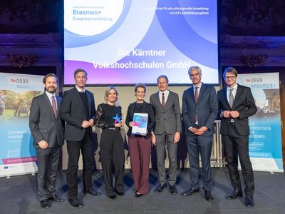 Gruppenfoto mit mehreren Personen in festlicher Kleidung auf einer Bühne im Hintergrund bunte Leinwand 