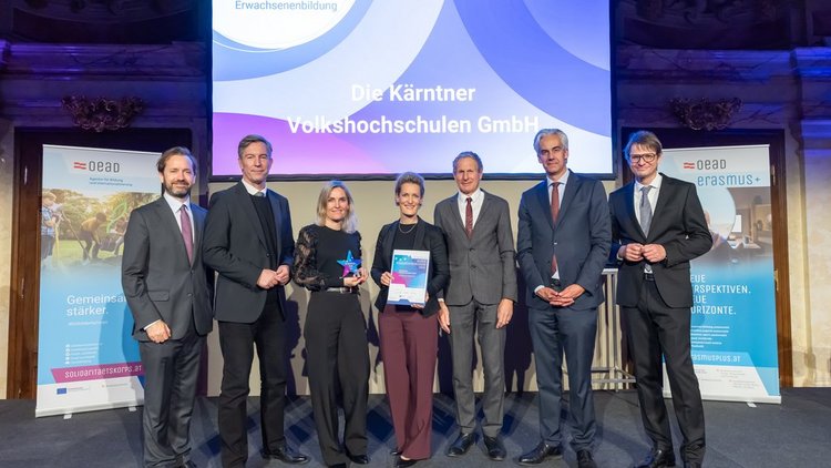Gruppenfoto mit mehreren Personen in festlicher Kleidung auf einer Bühne im Hintergrund bunte Leinwand 