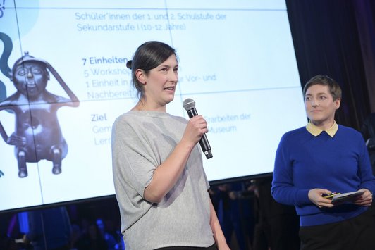Zwei Frauen stehen auf einer Bühne und präsentieren