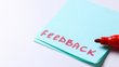 Das Wort Feedback steht in roter Schrift auf einem blauen Postit