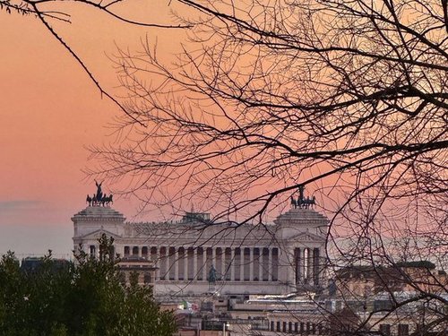 Malerische Aussicht auf das berühmte Vittoriano-Denkmal bei Sonnenuntergang in Rom, eingerahmt von Bäumen.