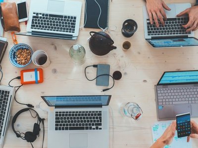 Tisch auf dem verschiedene Laptops stehen, an denen Personen arbeiten