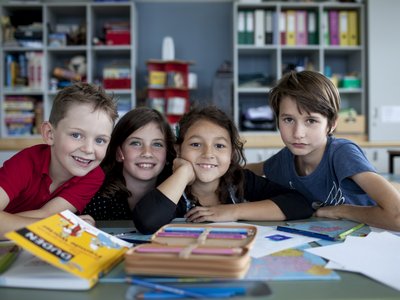 Kinder lächeln für ein Gruppenfoto in die Kamera, vor ihnen liegen Bücher