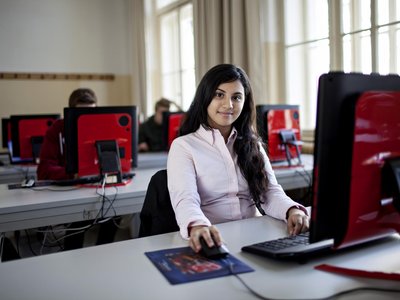 Mädchen sitzt in einer Schule vor einem Computer und sieht in die Kamera