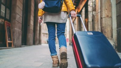 Eine Person mit einem Rucksack und einem Koffer geht eine Straße entlang.