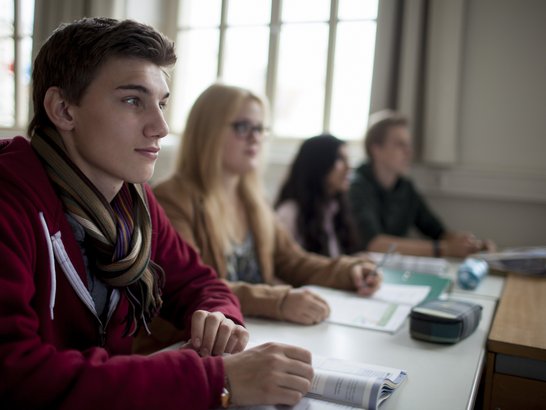 Vier Schüler und Schülerinnen lauschen aufmerksam dem Unterricht und blicken Richtung Tafel