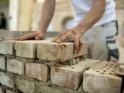 Ziegel werden von jungem Maurer zu einer Mauer aufgebaut