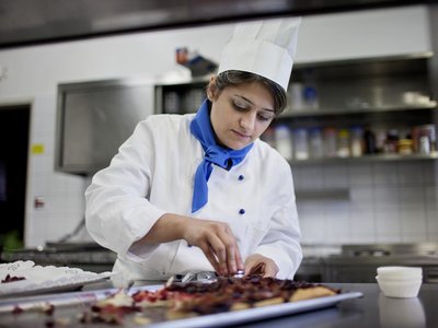 Junge Frau in Kochuniform garniert Essen in Küche