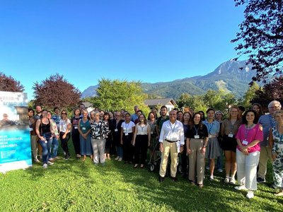 Gruppenfoto von vielen Leuten, die auf einer Wiese stehen. Im Hintergrund sieht man die Berge.