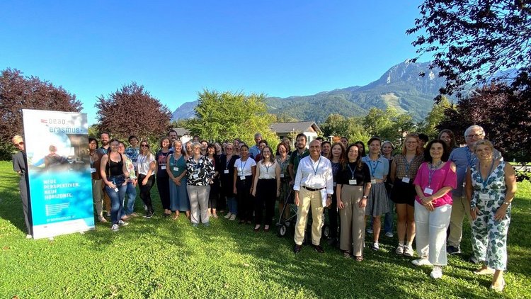 Gruppenfoto von vielen Leuten, die auf einer Wiese stehen. Im Hintergrund sieht man die Berge.