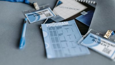 Ein Tagungsprogramm, ein Stift, zwei Namensschilder und ein Notizbuch liegen auf einer Oberfläche.