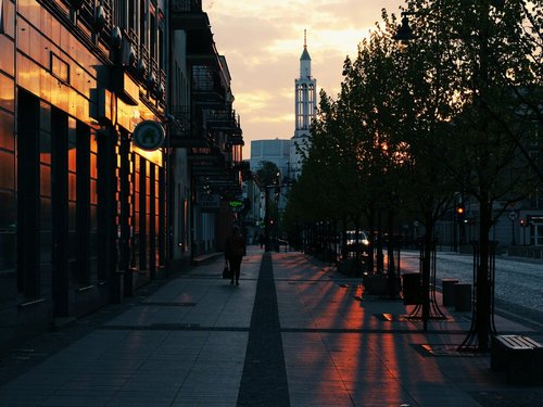 Person die auf grauem Gehsteig während der goldenen Stunde in Białystok geht.