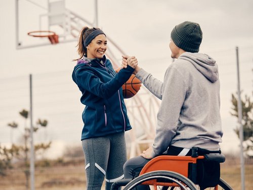 Male athlete with disability and his female friend congratulating each other after playing basketball on an outdoor court. Focus is on woman.