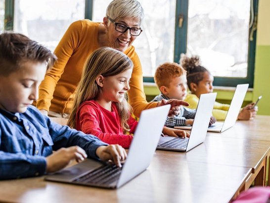 Lehrerin, die ihren Schüler/innen hilft, Laptops in der Klasse zu benutzen.