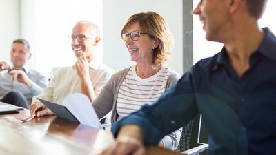 Vier Personen sitzen lächelnd an einem Tisch bei einer Besprechung