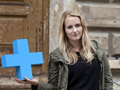 Junge Studentin mit blauem Plus vor Haus