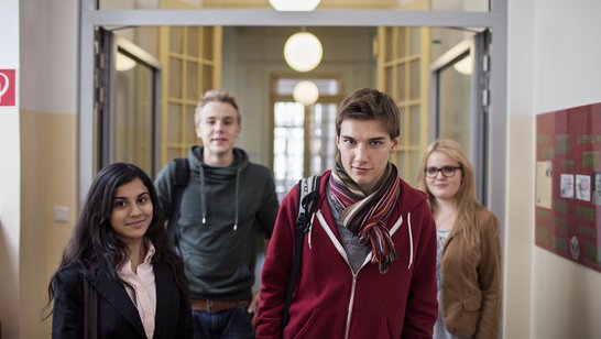 Schülergruppe Vier Schüler und Schülerinnen gehen in einem Schulgang der Kamera entgegen