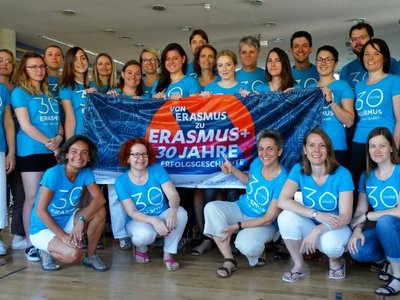 Gruppe an Menschen mit 30 Jahre Erasmus+ T-Shirt gekleidet halten gemeinsam die 30 Jahre Erasmus+ Flagge hoch