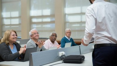 Vier Personen sitzen vor einem Laptop, vor ihnen ein Vortragender